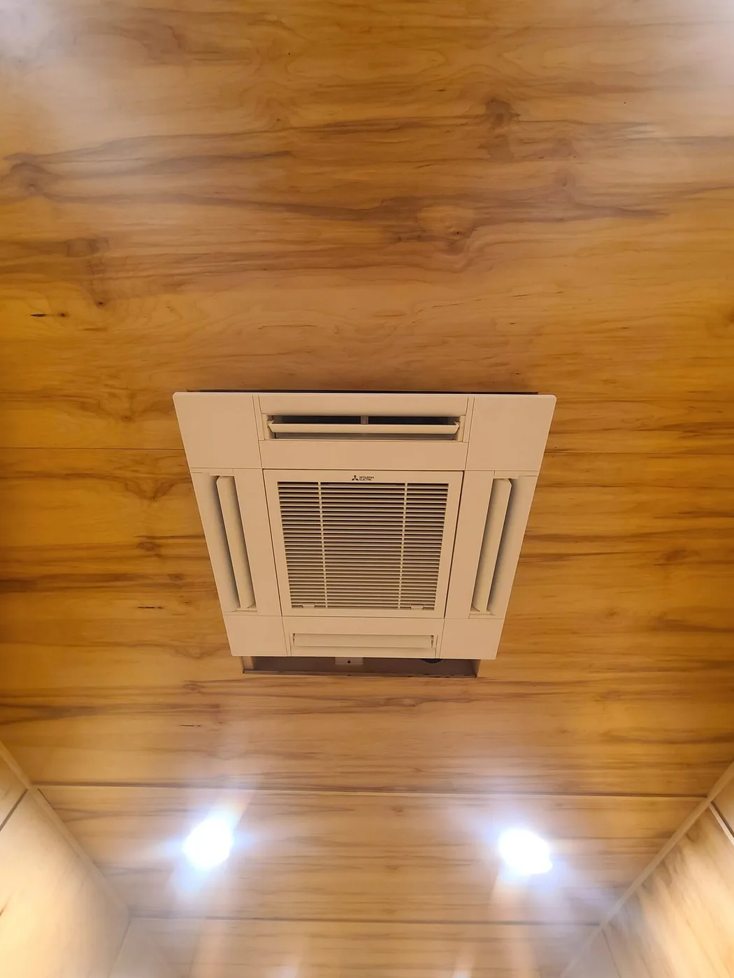 Mitsubishi four-way ceiling cassette heat pump head recessed into a wood-panelled ceiling